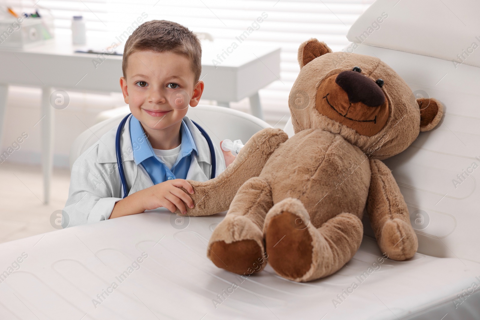 Photo of Little boy with stethoscope, syringe and toy pretending to be doctor indoors