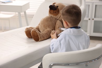 Photo of Little boy with stethoscope, syringe and toy pretending to be doctor indoors, back view