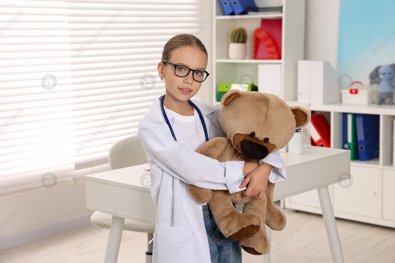 Photo of Girl with stethoscope and toy pretending to be doctor indoors