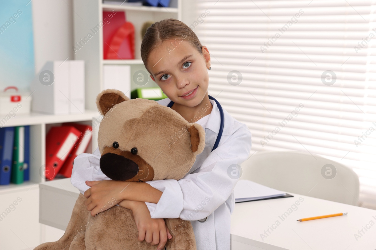 Photo of Girl with stethoscope and toy pretending to be doctor indoors