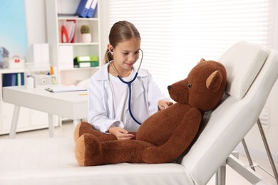 Photo of Girl with stethoscope and toy pretending to be doctor indoors