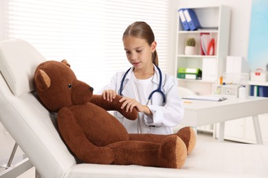 Photo of Girl with stethoscope and toy pretending to be doctor indoors