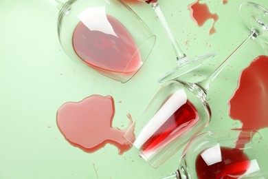 Photo of Glasses with spilled red wine on light green background, flat lay