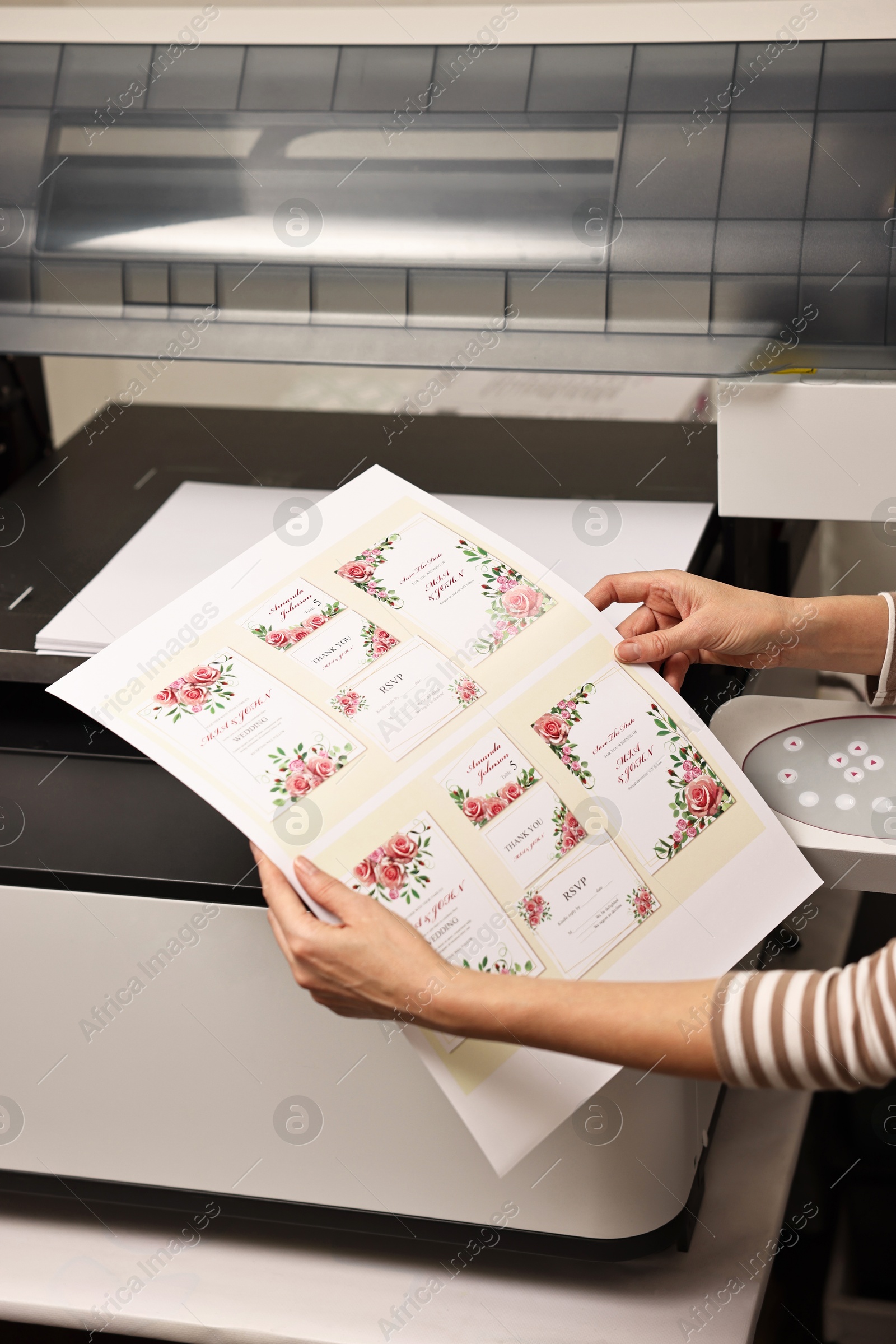 Photo of Woman with printed invitation cards near modern printer indoors, closeup. Printing house