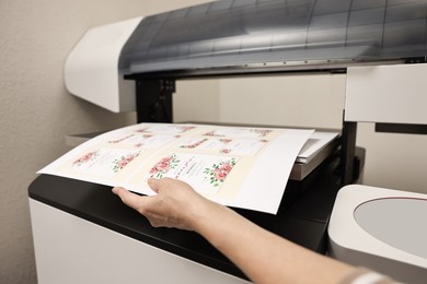 Photo of Woman using modern printer indoors, closeup. Printing house