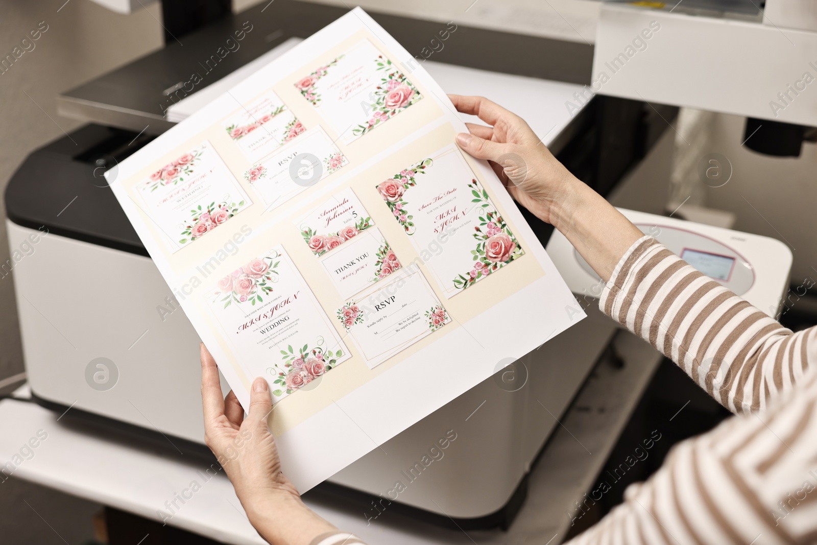 Photo of Woman with printed invitation cards near modern printer indoors, closeup. Printing house