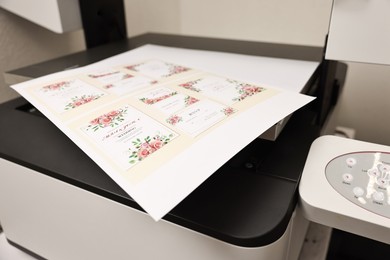 Photo of Modern printer with printed wedding invitation cards indoors, closeup. Printing house