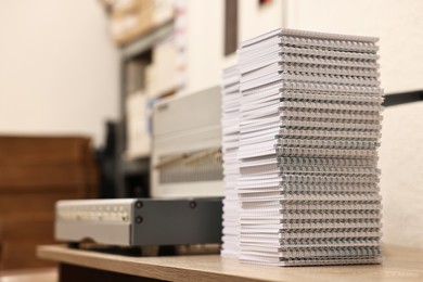 Photo of Modern binding machine and stacks of notebooks on wooden table indoors, selective focus