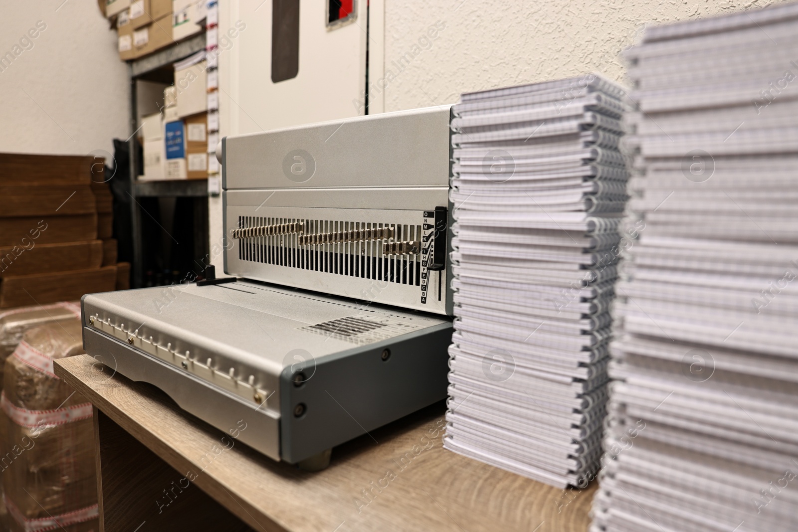 Photo of Modern binding machine and stacks of notebooks on wooden table indoors