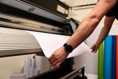 Photo of Man using wide-format printer indoors, closeup. Printing house