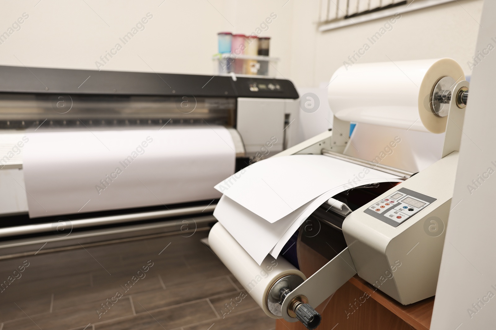 Photo of Modern roll laminator with paper on desk indoors. Printing house