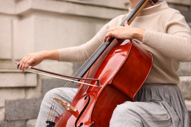 Photo of Young woman playing cello on stairs outdoors, closeup. Classic musical instrument