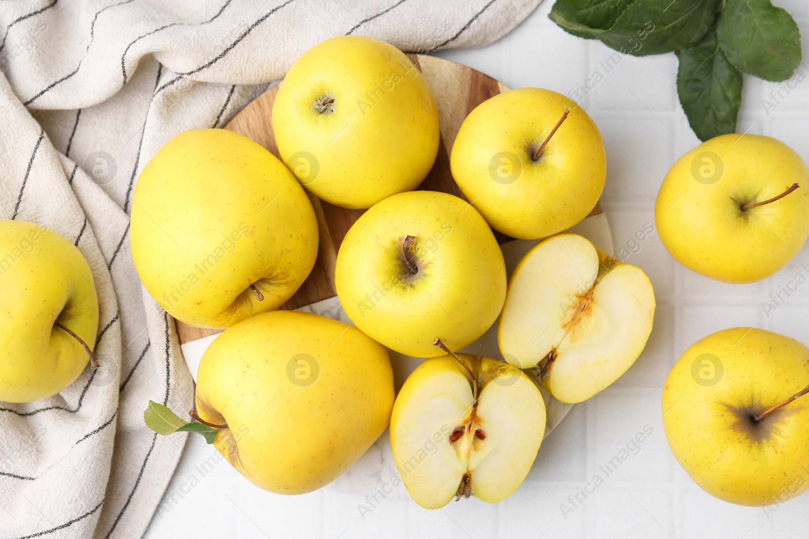 Photo of Fresh ripe yellow apples and green leaves on white tiled table, flat lay