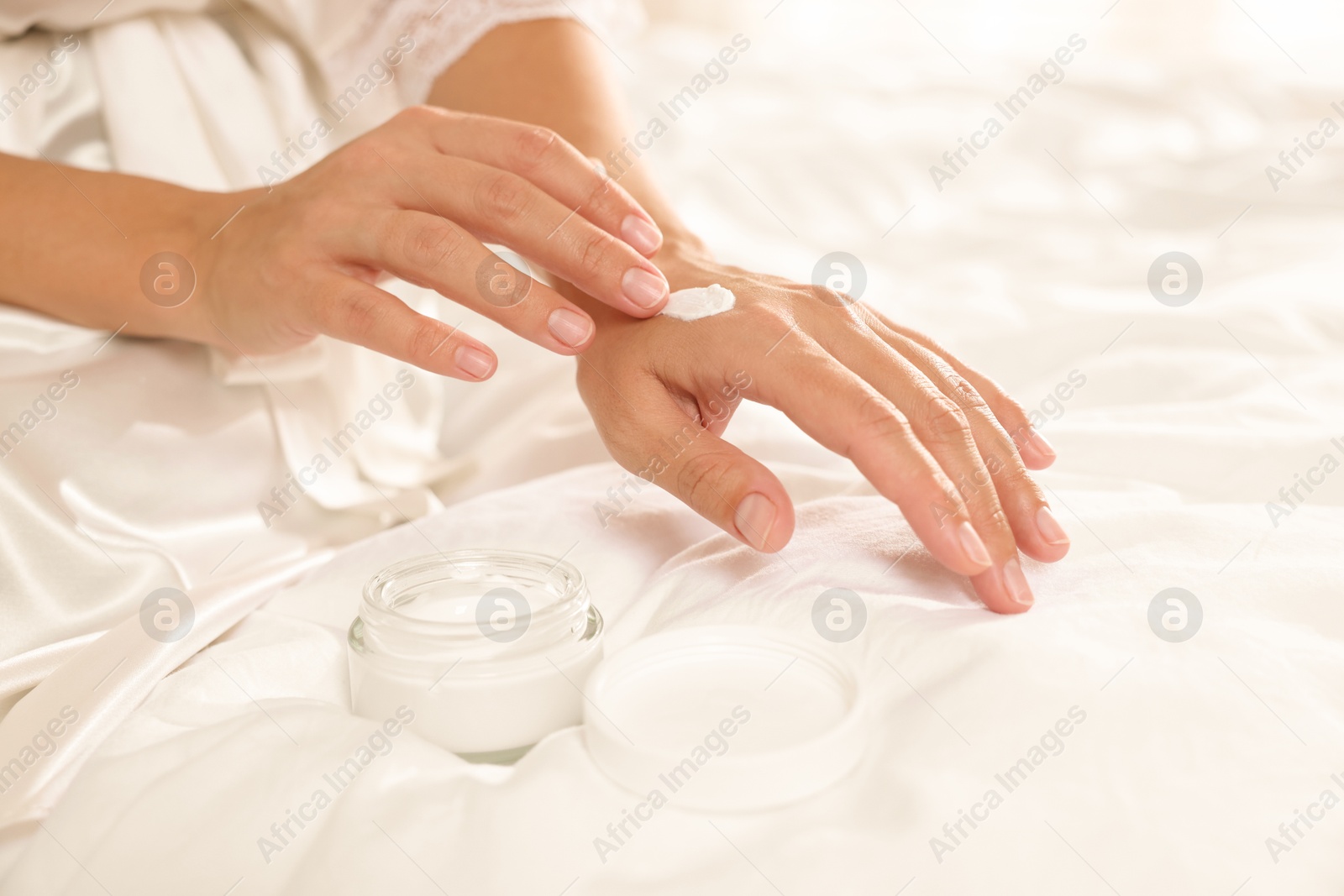 Photo of Woman applying cream onto hand on bed at home, closeup