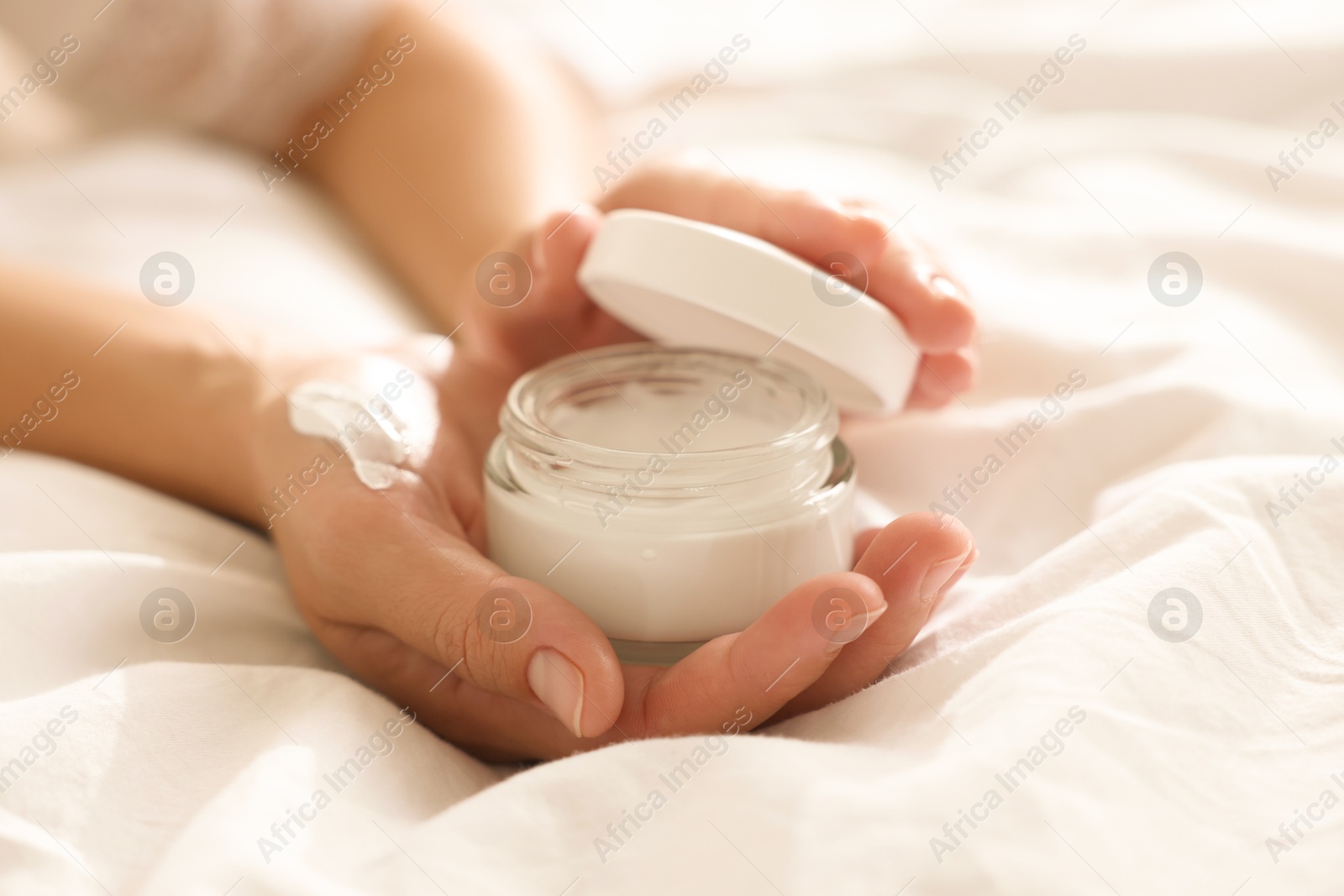 Photo of Woman with jar of cream on bed at home, closeup