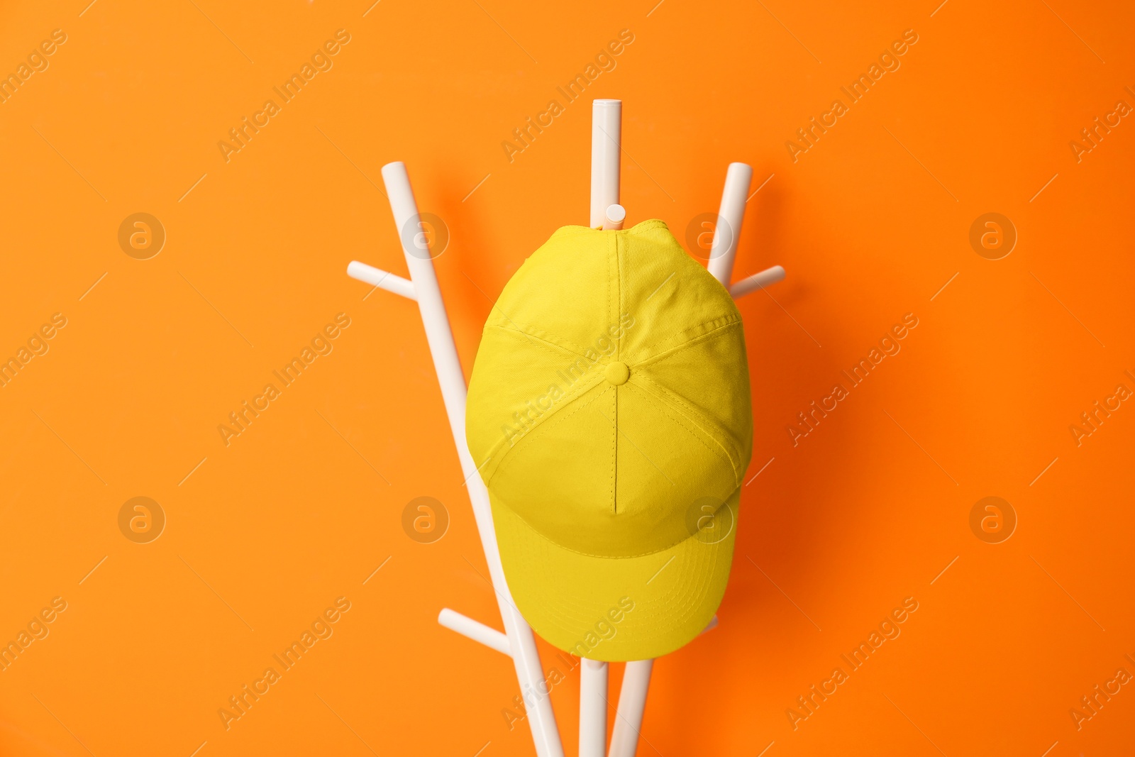 Photo of Stylish baseball cap on coat rack against orange wall. Mockup for design