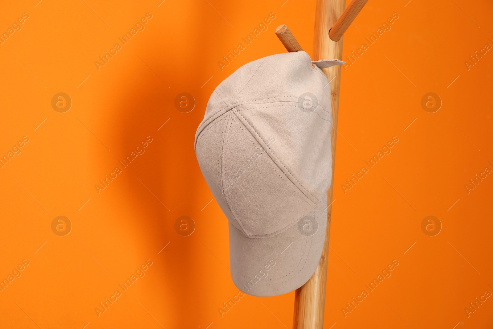 Photo of Stylish baseball cap on coat rack against orange wall. Mockup for design