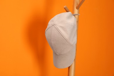 Photo of Stylish baseball cap on coat rack against orange wall. Mockup for design