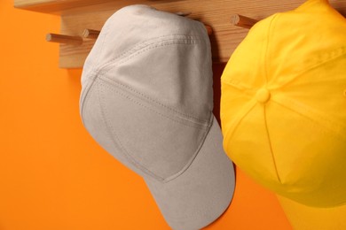 Photo of Stylish baseball caps on orange wall, closeup. Mockup for design