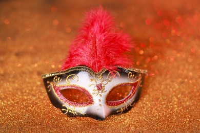 Photo of Beautiful carnival mask on shiny color background, closeup