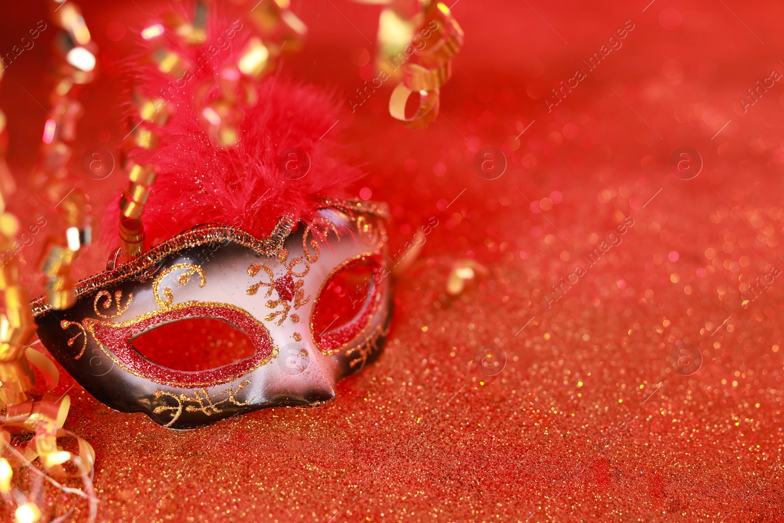 Photo of Beautiful carnival mask on shiny red background, closeup. Space for text