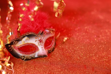 Photo of Beautiful carnival mask on shiny red background, closeup. Space for text