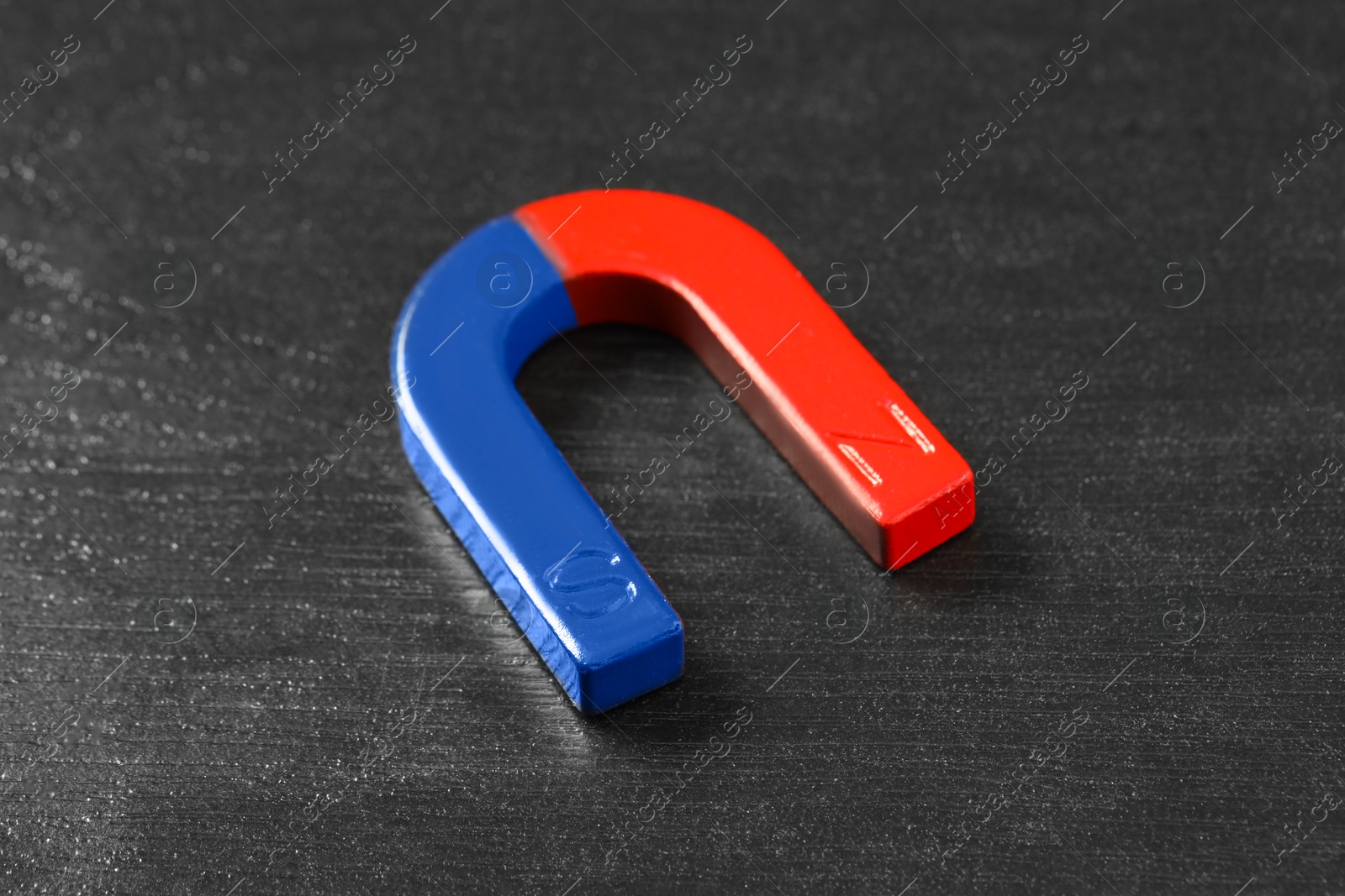 Photo of One horseshoe magnet on black wooden table, closeup