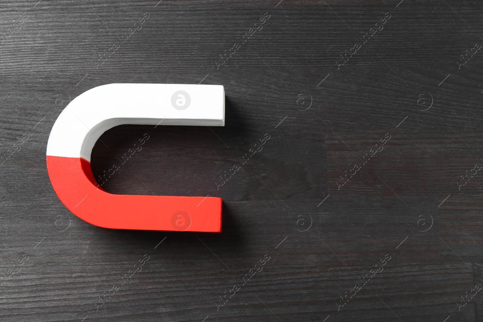 Photo of One horseshoe magnet on black wooden background, top view. Space for text