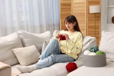 Beautiful woman knitting on sofa at home