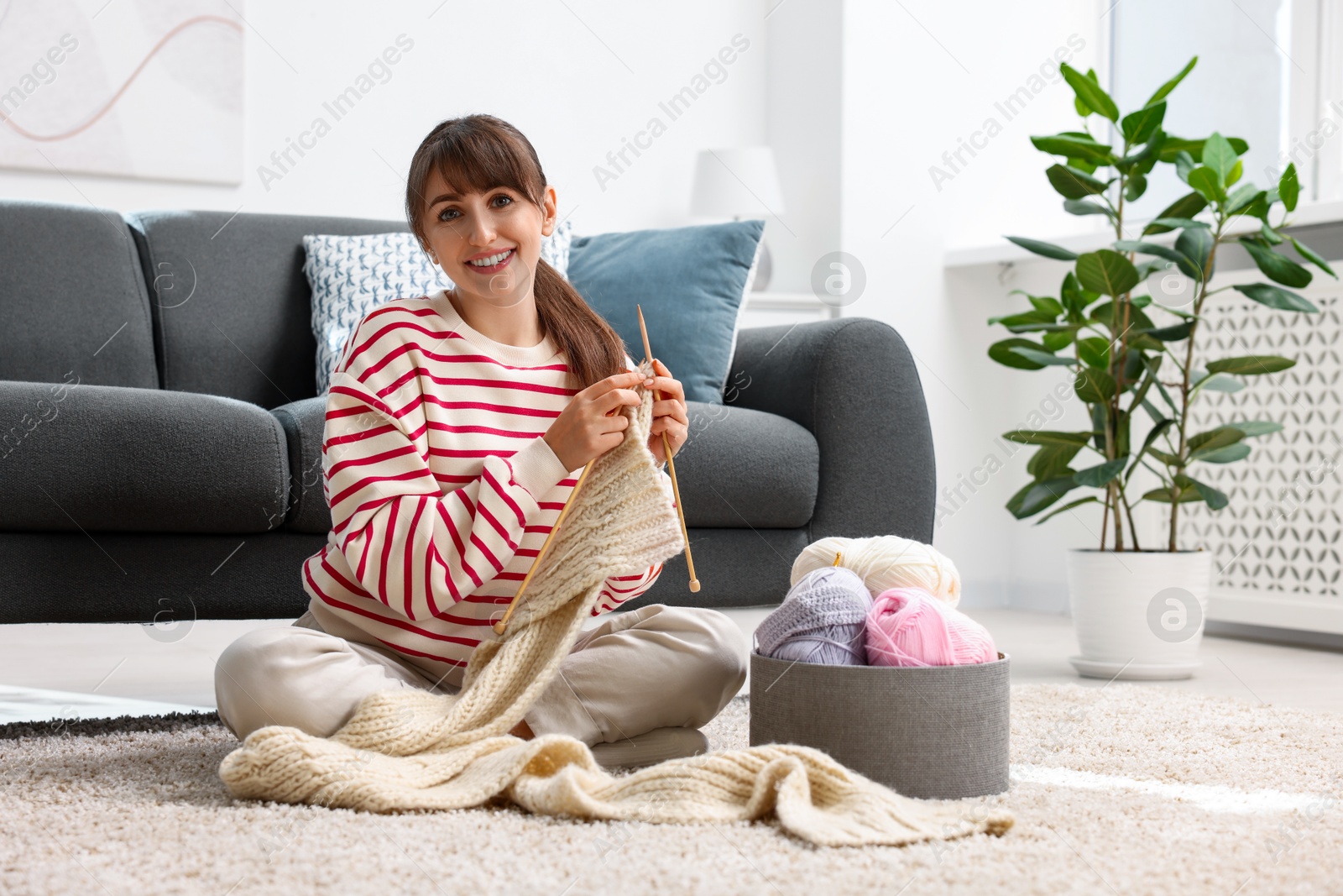 Photo of Beautiful woman knitting with needles on floor at home