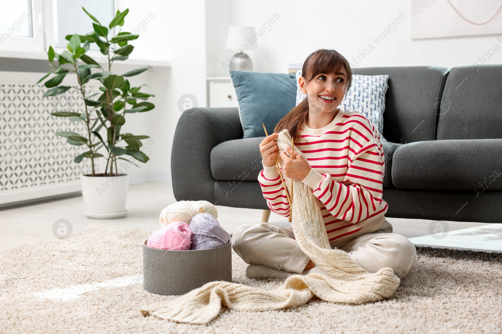 Photo of Beautiful woman knitting with needles on floor at home