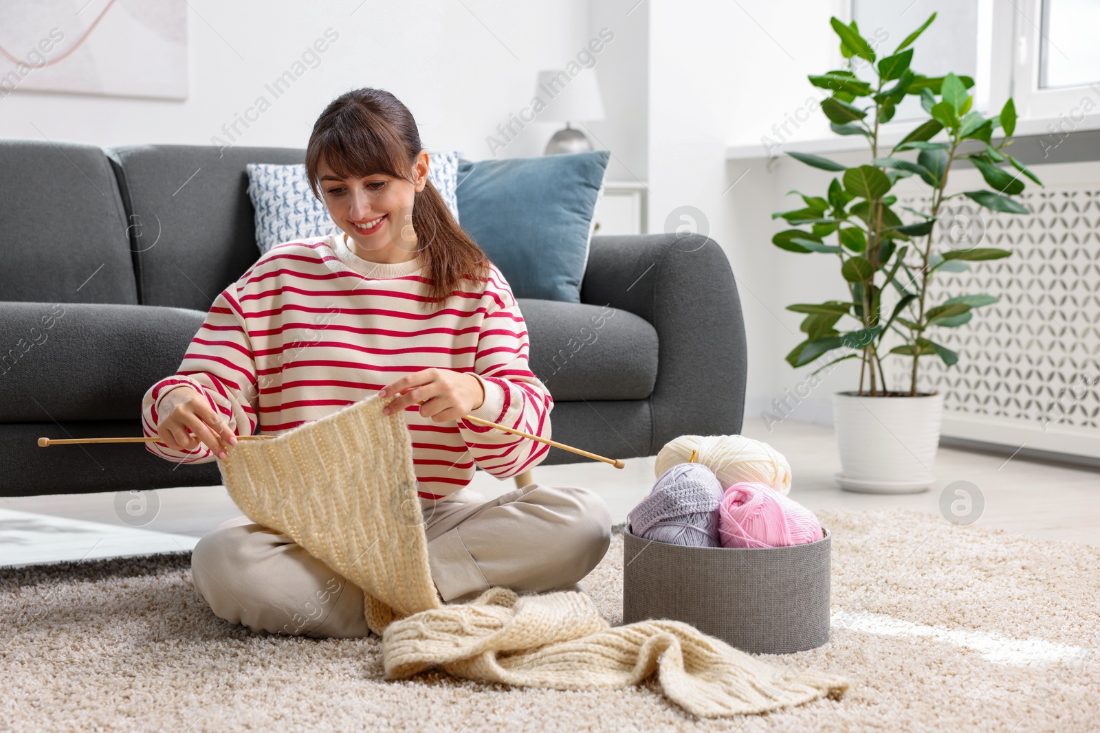 Photo of Beautiful woman knitting with needles on floor at home