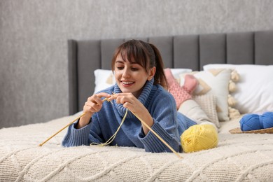 Photo of Beautiful woman knitting with needles on bed at home