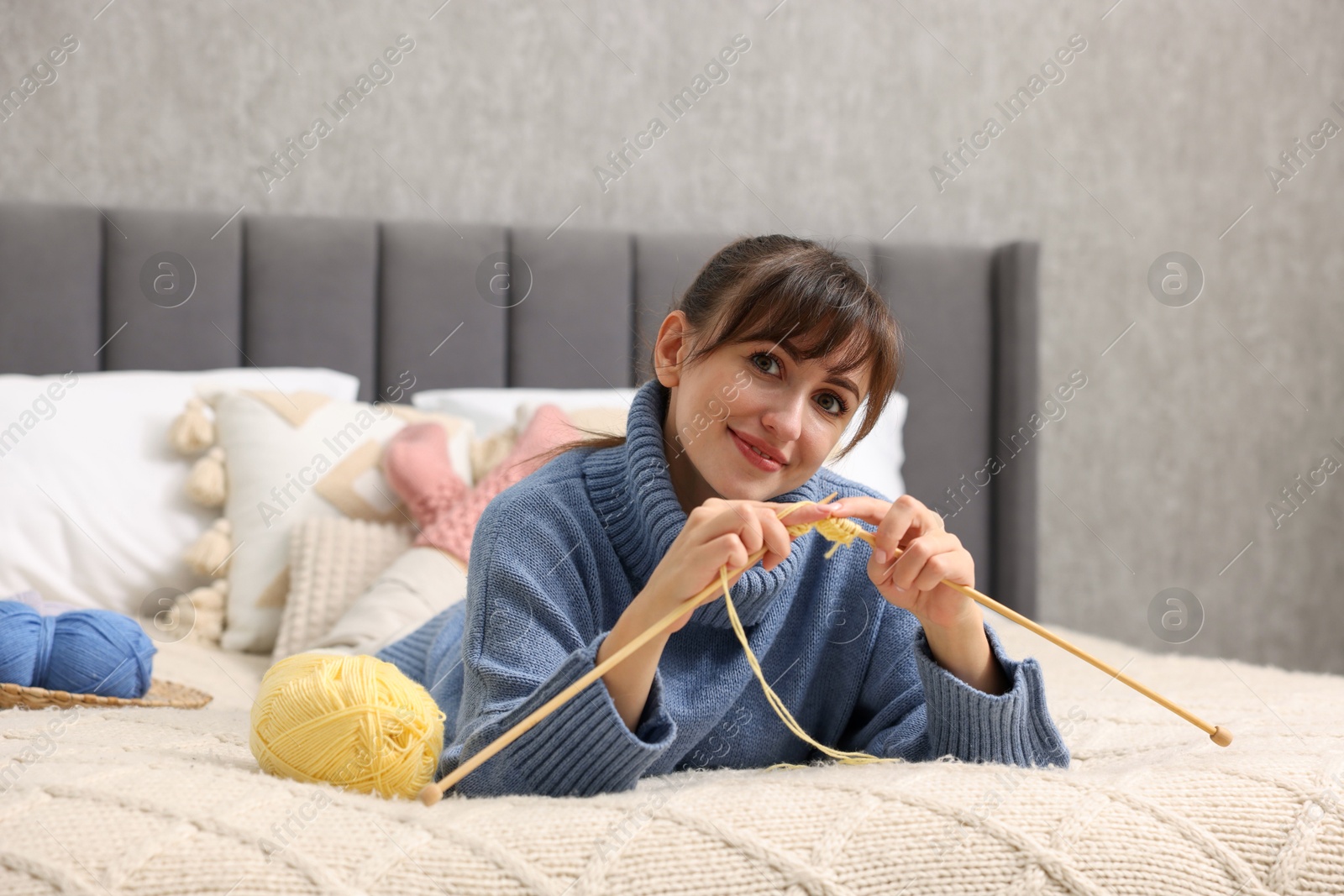 Photo of Beautiful woman knitting with needles on bed at home