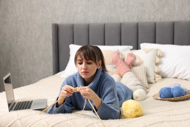 Photo of Woman learning to knit with online course on bed at home