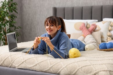 Woman learning to knit with online course on bed at home