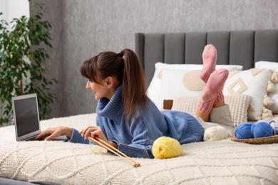 Woman learning to knit with online course on bed at home