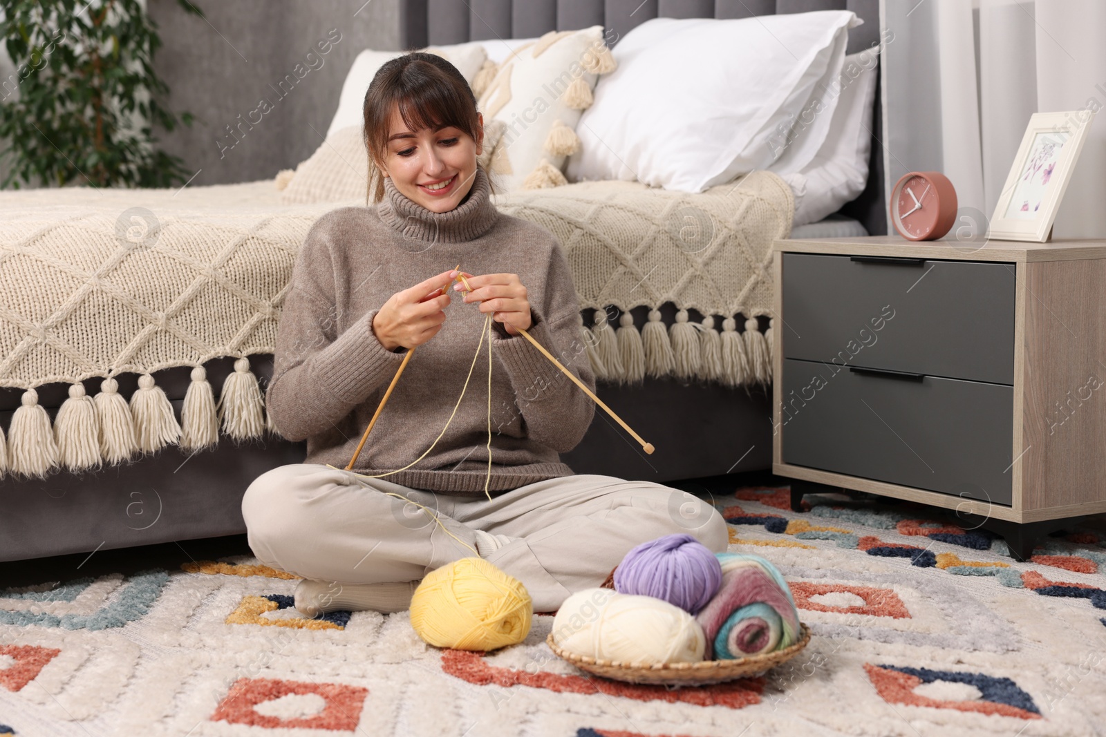 Photo of Beautiful woman knitting with needles on floor at home