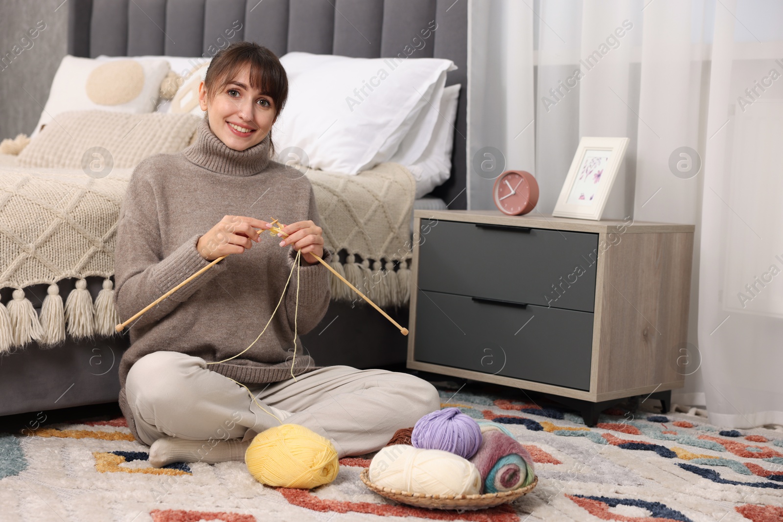 Photo of Beautiful woman knitting with needles on floor at home