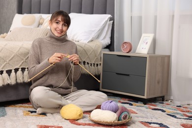 Photo of Beautiful woman knitting with needles on floor at home