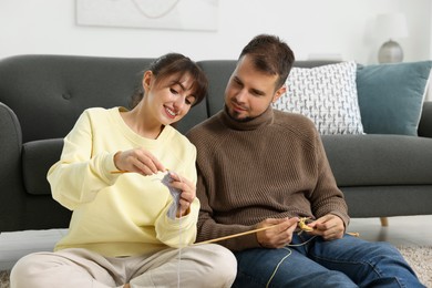 Photo of Woman teaching her boyfriend how to knit on floor at home