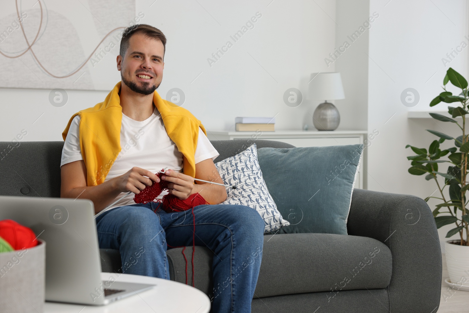 Photo of Man learning to knit with online course on sofa at home