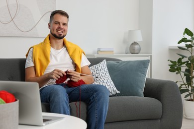 Man learning to knit with online course on sofa at home