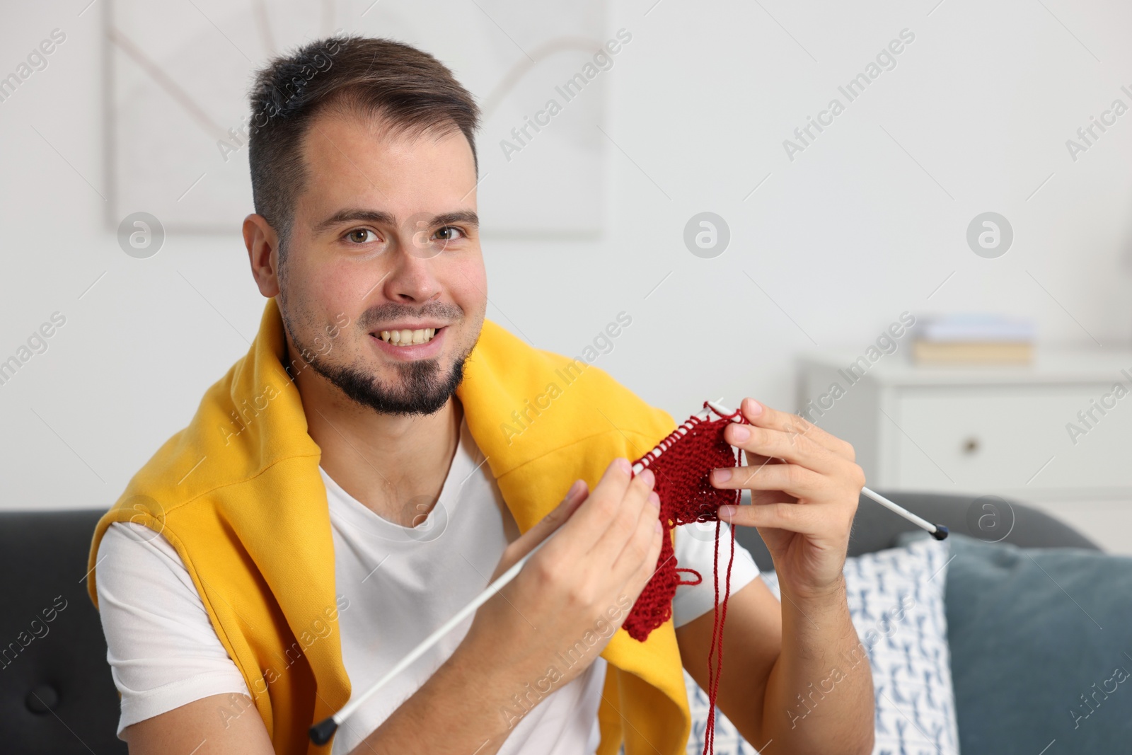 Photo of Man knitting with needles on sofa at home