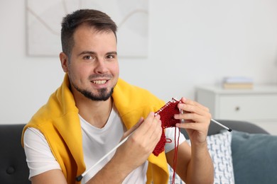 Man knitting with needles on sofa at home