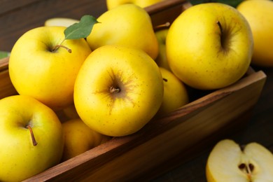 Photo of Ripe yellow apples in wooden crate on table, closeup