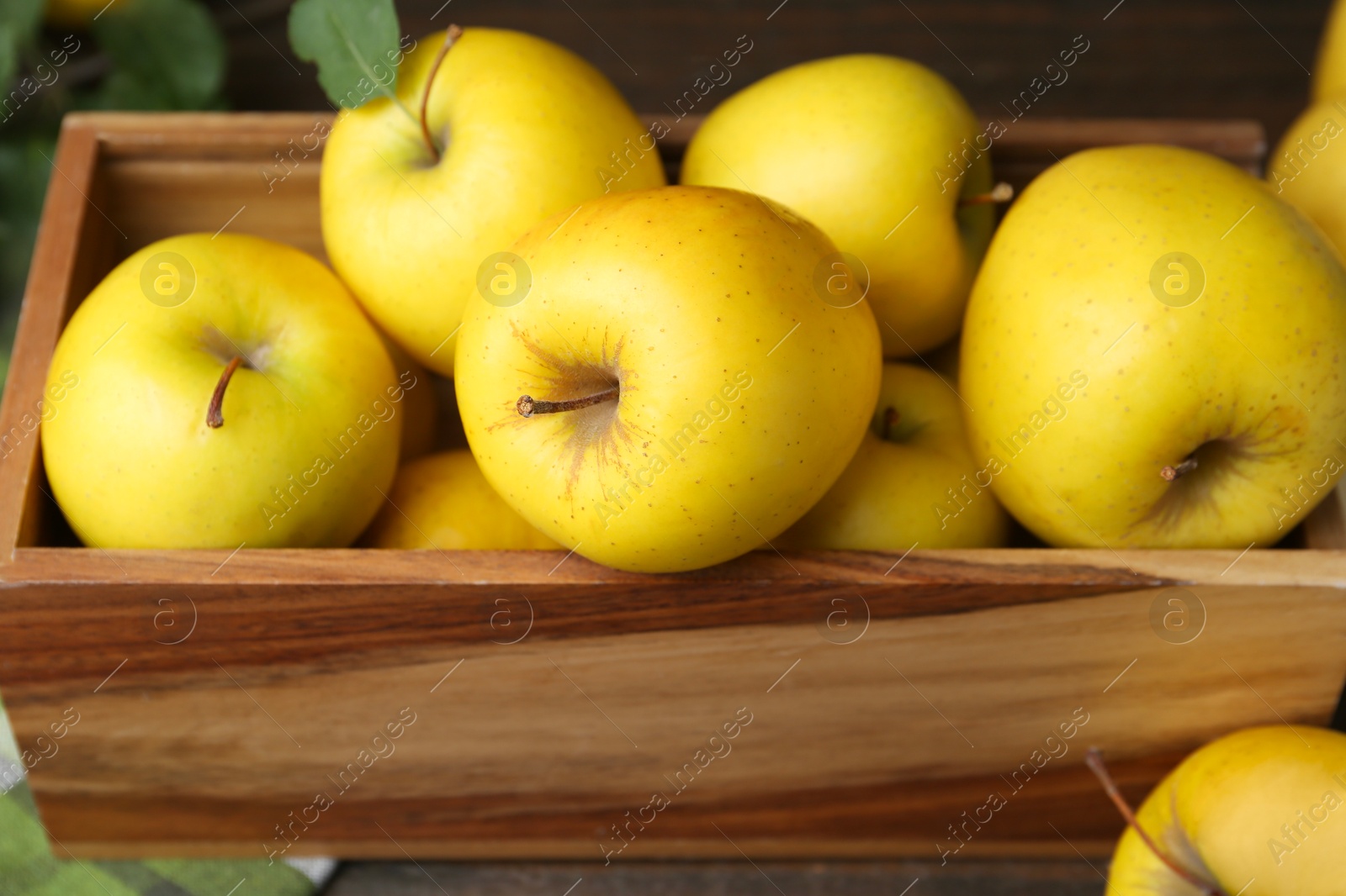 Photo of Ripe yellow apples in wooden crate on table, closeup