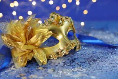 Photo of Beautiful carnival mask on blue glitter background against blurred lights, closeup. Bokeh effect