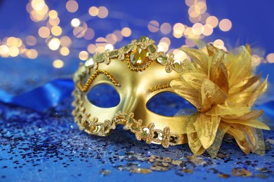 Photo of Beautiful carnival mask on blue glitter background against blurred lights, closeup. Bokeh effect