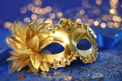 Photo of Beautiful carnival mask on blue glitter background against blurred lights, closeup. Bokeh effect